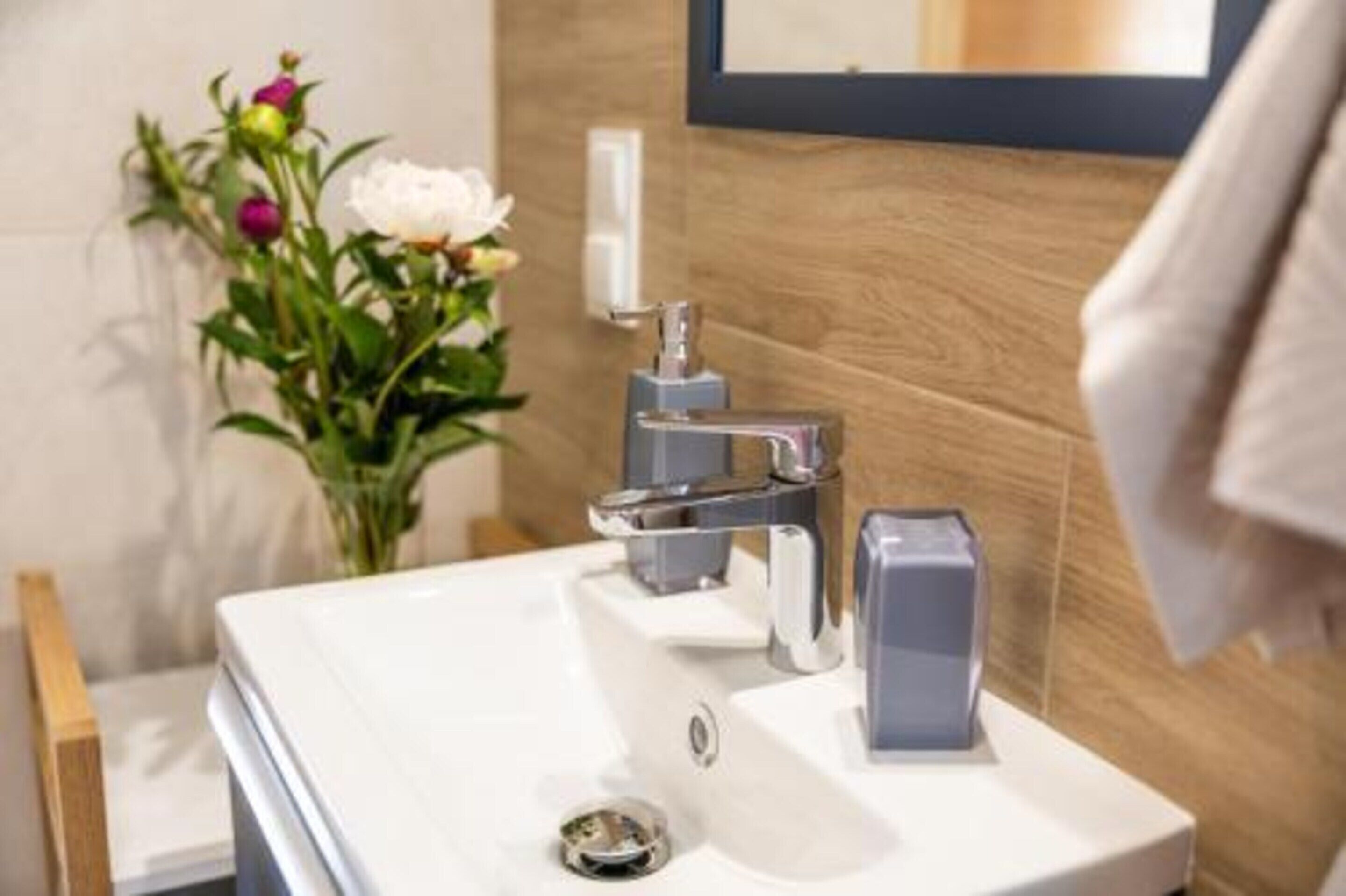 Un bagno moderno con lavabo bianco, rubinetteria cromata e una parete in legno.
