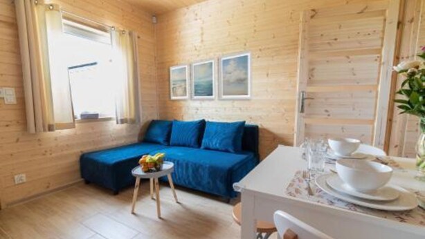 A wooden interior with a sofa, a small round table with a fruit bowl, and a dining table set for two. - Comfortable Holiday Homes in Mielno (Mielno)