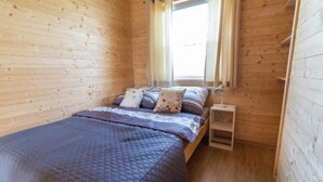 A wooden-paneled room with a bed, a small bedside table, and a window. - Comfortable Holiday Homes in Mielno (Mielno)