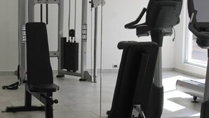 Et fitnesscenter med forskellig træningsudstyr, herunder bænkpres, løbebånd og vægtmaskine.
