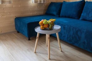 Una habitación con un sofá azul, un taburete de madera redondo y una cesta de frutas, y un piso de madera.