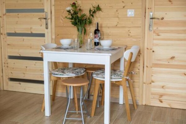 Un interior de madera con una mesa y sillas blancas, un jarrón con flores y una botella.