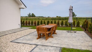 Une terrasse avec une table et des chaises, un chemin de gravier et une vue sur un champ.