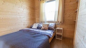 Une petite pièce en bois, avec un lit, une table de chevet et une fenêtre.