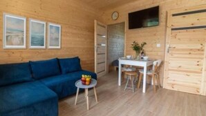 Een gezellige kamer met een blauwe bank, een klein rond tafeltje met fruit, een witte tafel met stoelen en houten wanden.