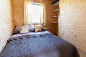 Una habitación pequeña y acogedora con una cama, una mesita de noche y una ventana con cortinas.