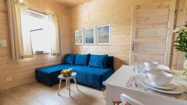 Een gezellige kamer met houten inrichting, een blauwe bank, een klein rond tafeltje met fruit, en een eethoek met wit servies.