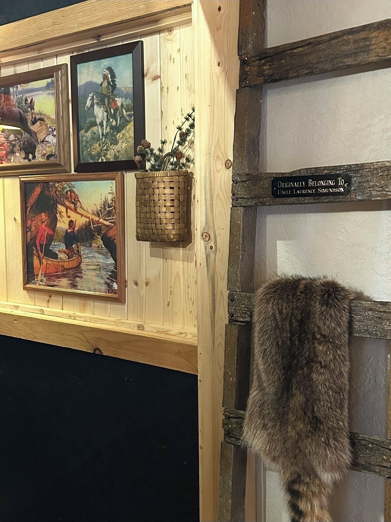 Una pared de madera con cuadros enmarcados, una cesta tejida y un letrero que indica la propiedad original de la habitación.