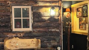 A rustic cabin interior with a wooden bench, a welcome sign, and a lantern.