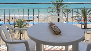 A balcony with a view of the beach, white plastic chairs, and a table with a tray of food. - Calafell beachfront apartment with swimming pool (Calafell)