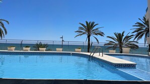 A clear blue sky, a swimming pool with a tiled edge, and palm trees. - Calafell beachfront apartment with swimming pool (Calafell)