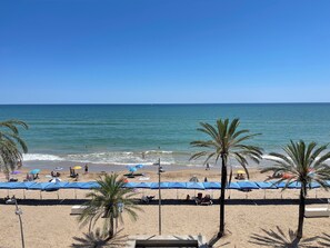 A beach with palm trees, umbrellas, and people. - Beachfront Apartment in Calafell with a Pool (Calafell)