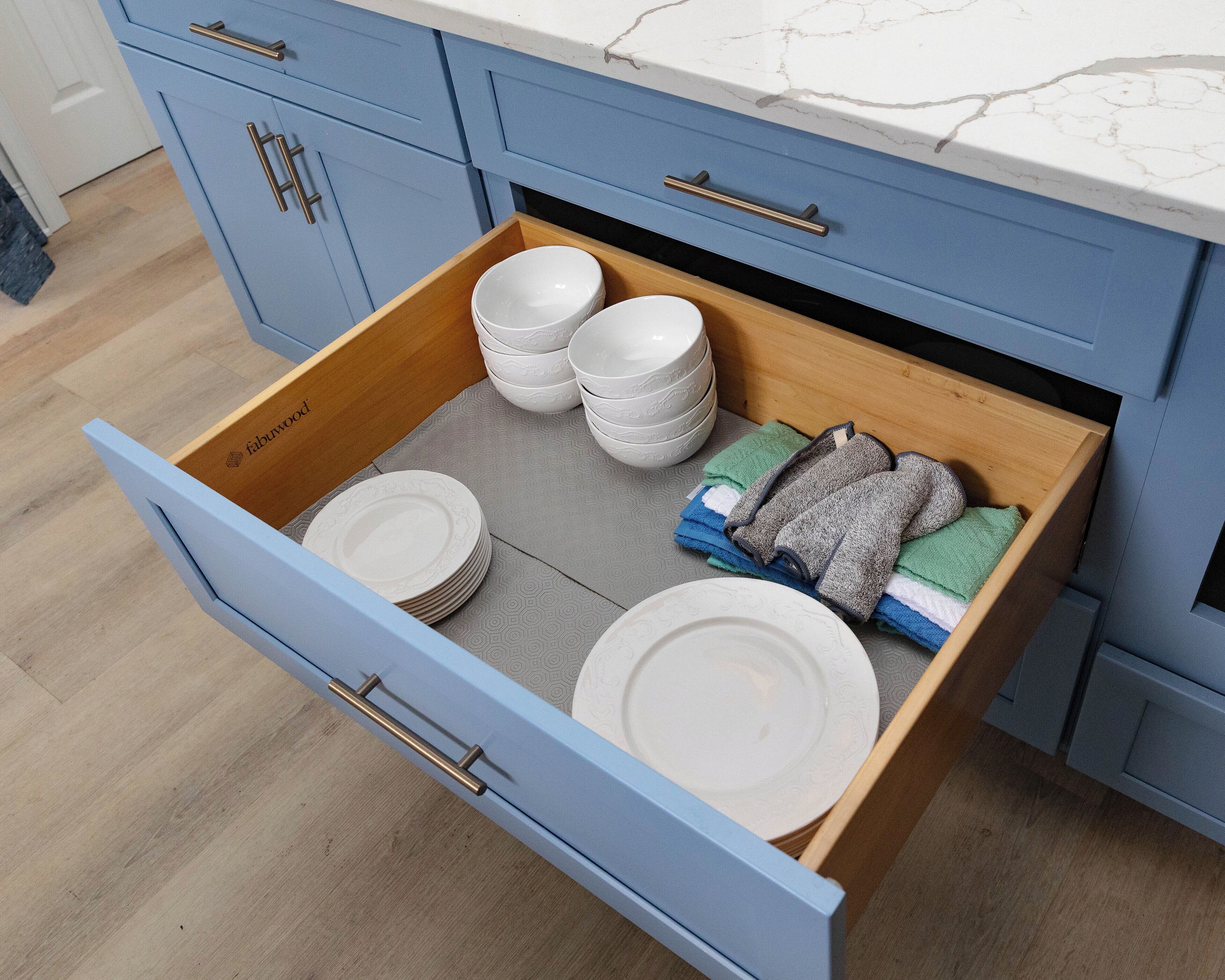 A kitchen drawer with stacked white plates and folded towels.