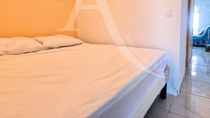 A bedroom with a bed, a white wall, and a door leading to another room. - Studio 4 personnes, terrasse vue mer et parking (Sète)
