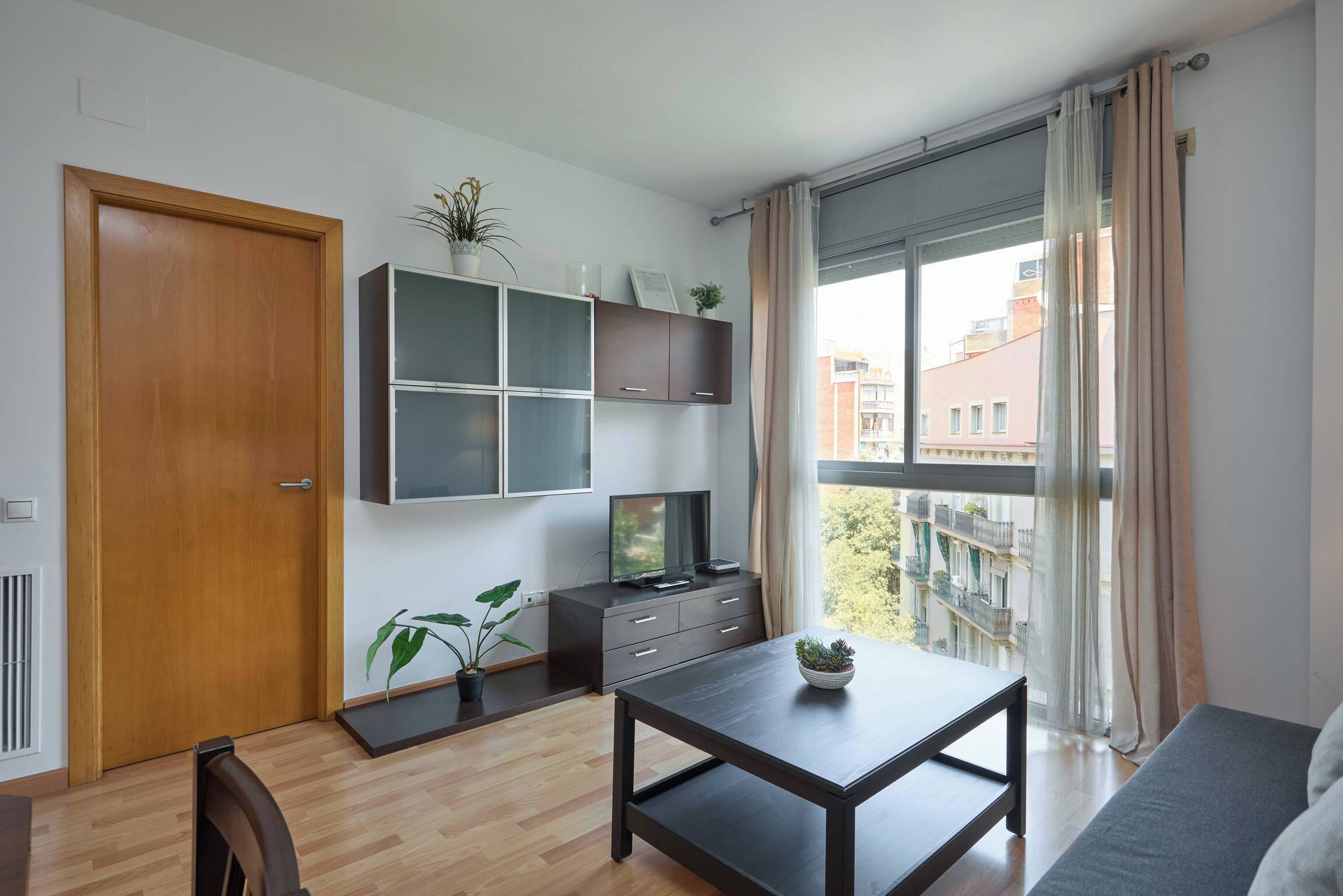 Una sala de estar moderna con puerta de madera, televisor sobre un mueble, mesa de comedor y sofá.
