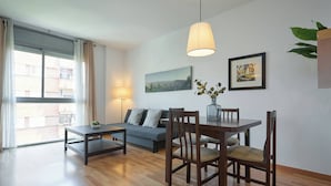Ein modernes Wohnzimmer mit einer Couch, einem Esstisch, Stühlen, einer Lampe und einem großen Fenster.