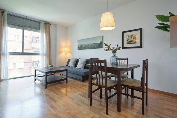 Un salon moderne comprenant un canapé, une table à manger, des chaises, une lampe et une grande fenêtre.