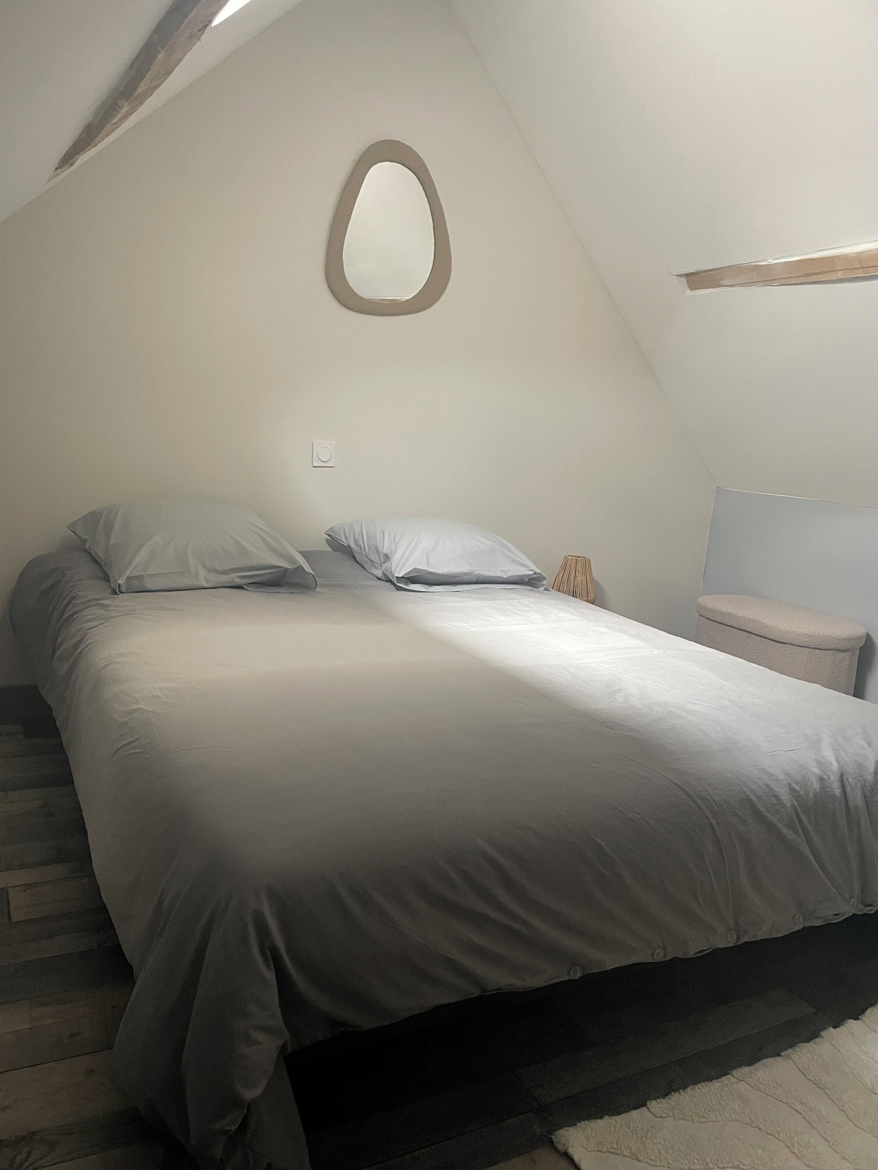 A bedroom with a bed, pillows, a nightstand, a mirror, and a window.