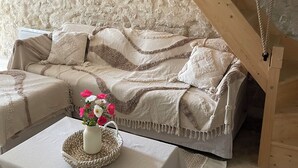 A cozy room with a wooden ceiling, a cushioned sofa, a small table with a vase of flowers, and a textured wall.