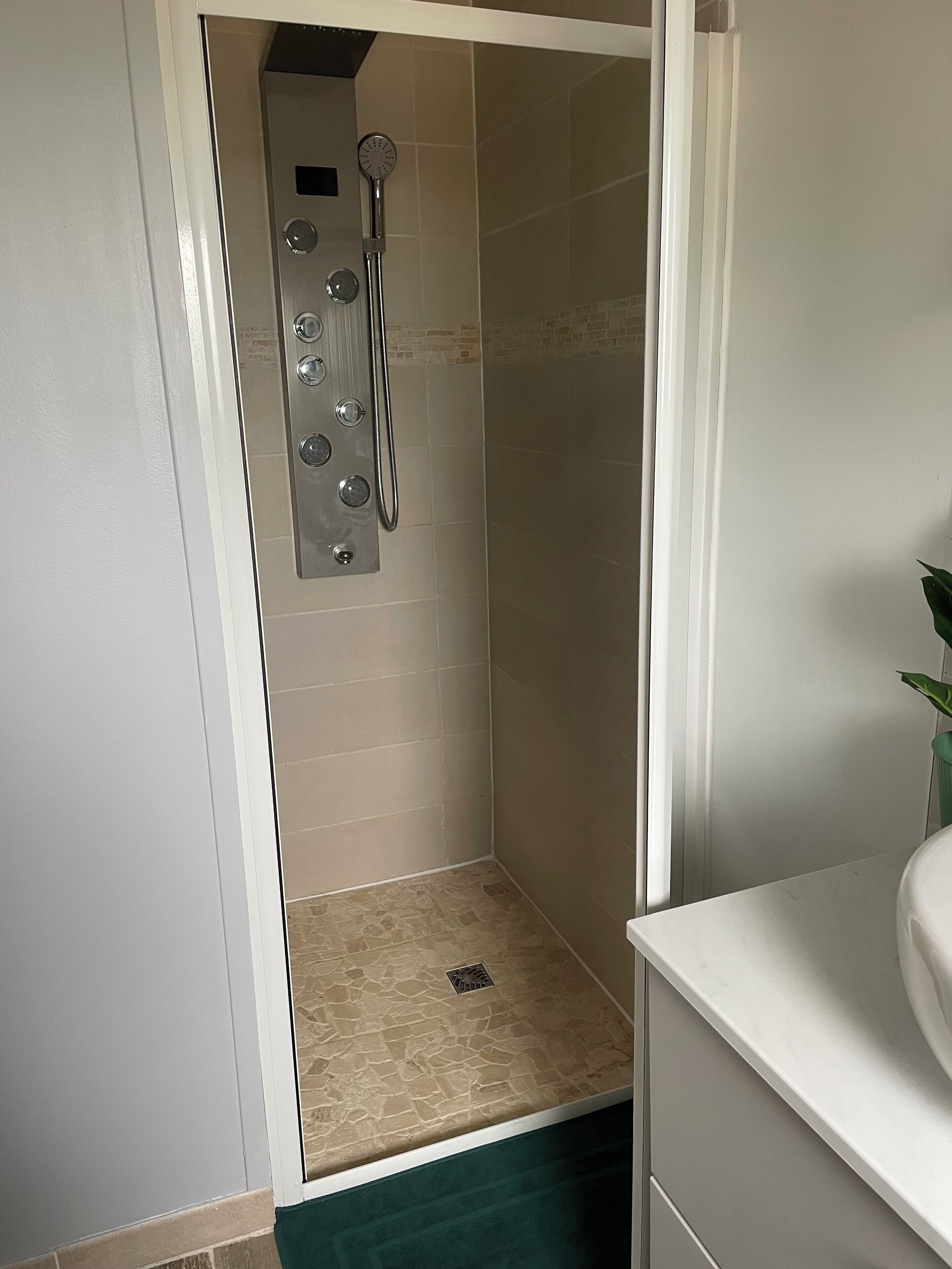 A small, enclosed shower area with a control panel and a handheld showerhead.