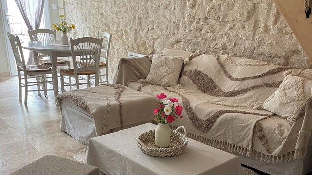 A cozy living room with a beige sofa, a coffee table with a vase of flowers, and a dining area with a white table and chairs.
