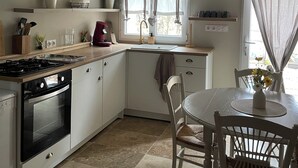 A compact kitchen with a stove, oven, and sink. There is a dining table with chairs and a clock on the wall.