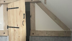 A bedroom with a wooden door, a bed, a small bench, and a sloped ceiling.