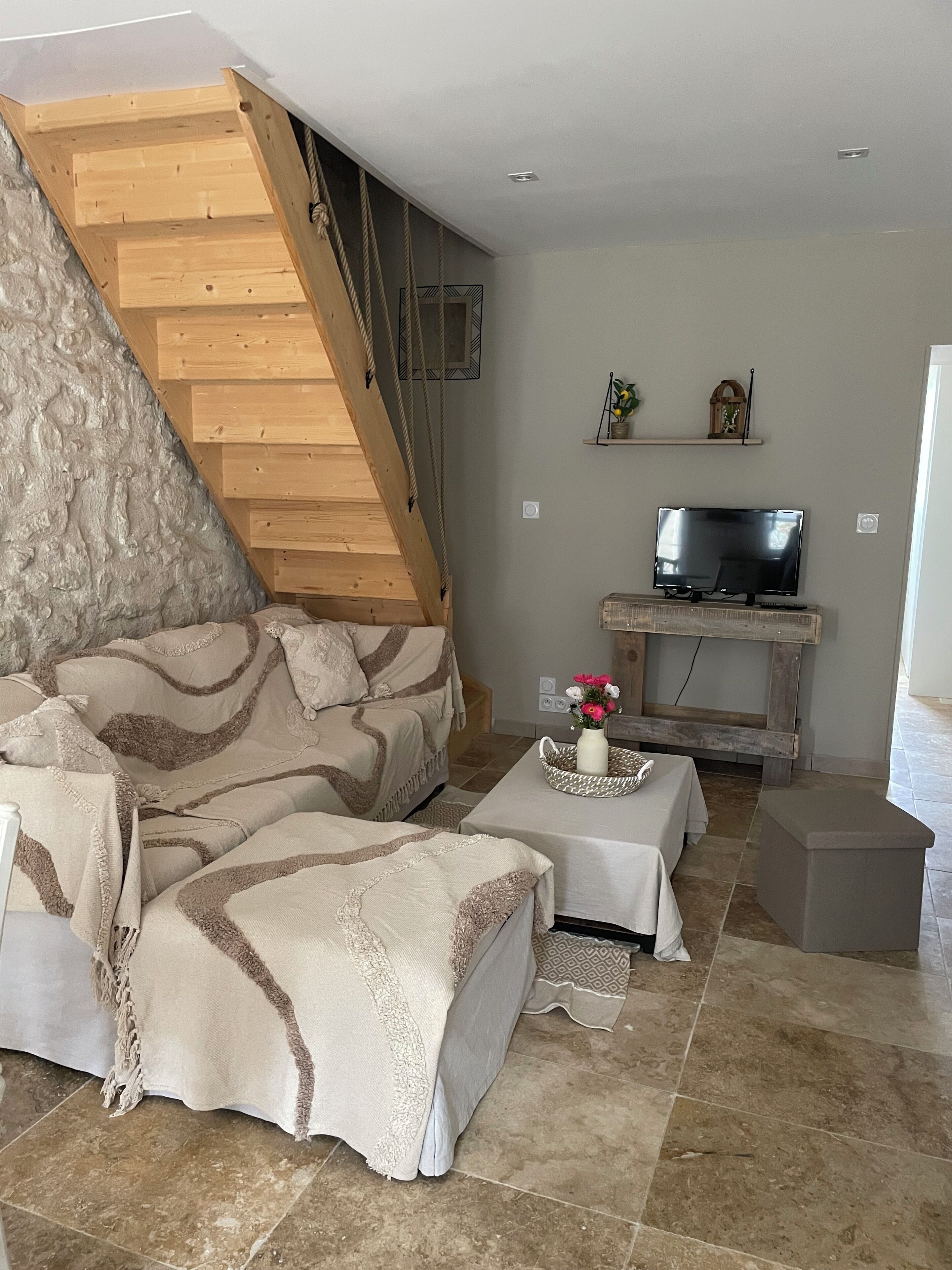 Un salon chaleureux avec un escalier en bois, un canapé, une table basse et un téléviseur.