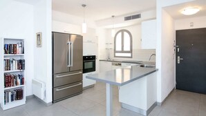 Una cocina moderna con refrigerador, horno y lavaplatos integrados. Hay una pequeña isla con una lámpara colgante arriba.