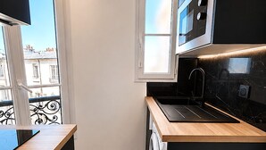 A compact kitchen with a washing machine, a microwave, and a window providing natural light.