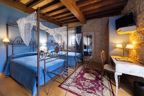 Un lit à baldaquin avec une couvre-lit bleue, un bureau avec une lampe et un mur en pierre.