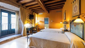 A hotel room with two beds, wooden beams, a stone wall, a window with curtains, a desk with a lamp, and a painting on the wall. - ABADIA CALDARIA (Arnoia)