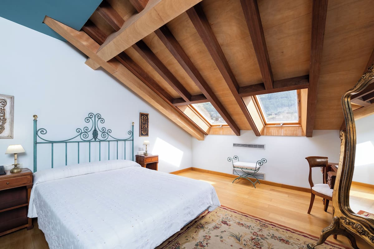 A bedroom with a wooden ceiling, a bed, a chair, a desk, and a large mirror.