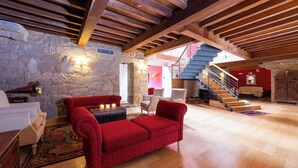 A spacious living area with a red sofa, wooden beams, stone walls, and a staircase leading to an upper level. - ABADIA CALDARIA (Arnoia)
