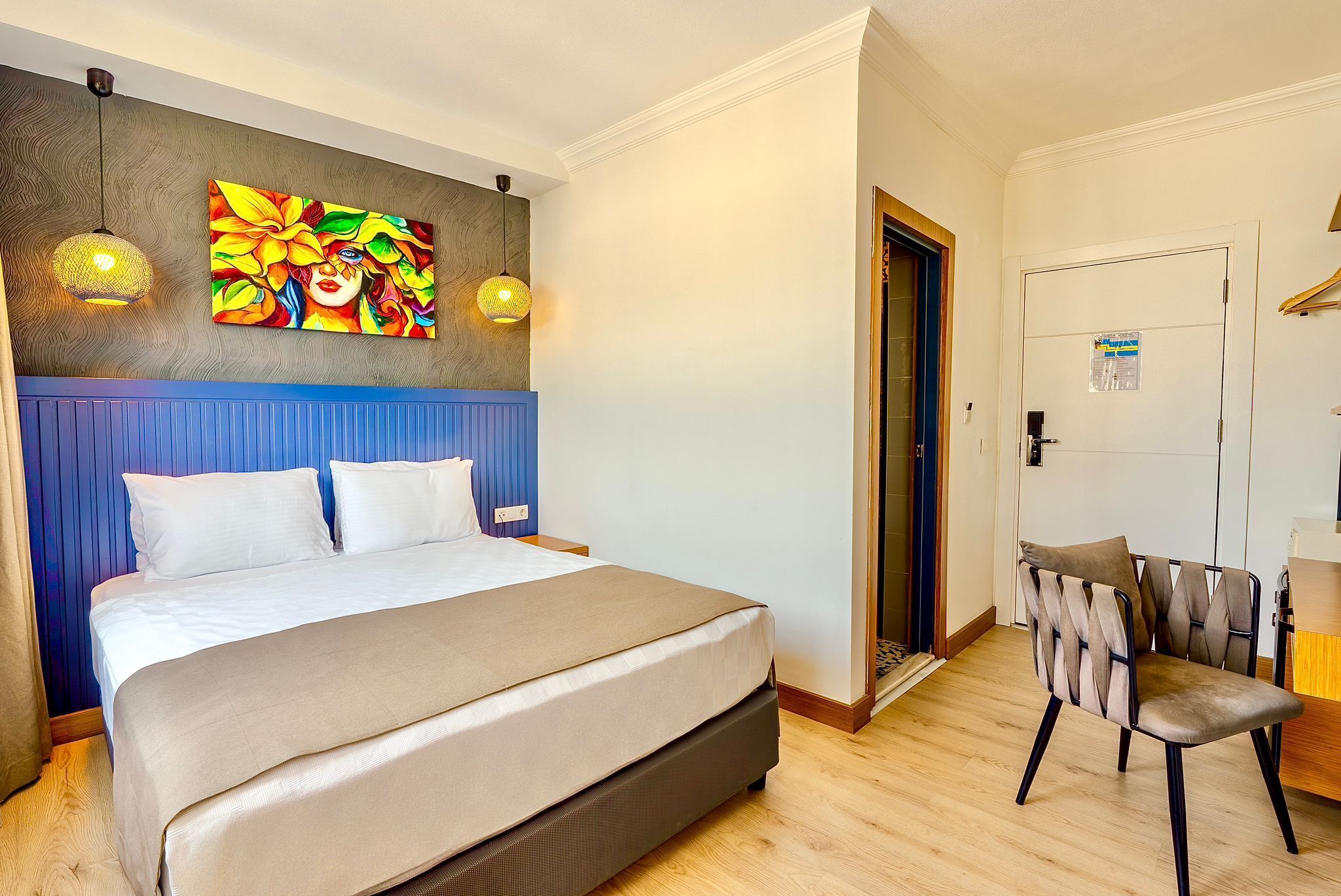 A hotel room with a large bed, a chair, a painting on the wall, and a door.