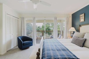 A bedroom with a bed, a chair, a nightstand, a lamp, and a view of the outdoors. - Fly Creek Collection - Watersound (Fairhope)