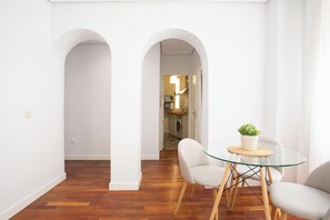 Ein modernes Interieur mit einer Essecke, die einen Glastisch und Stühle, einen Blumentopf und eine sichtbare Küche im Hintergrund umfasst.