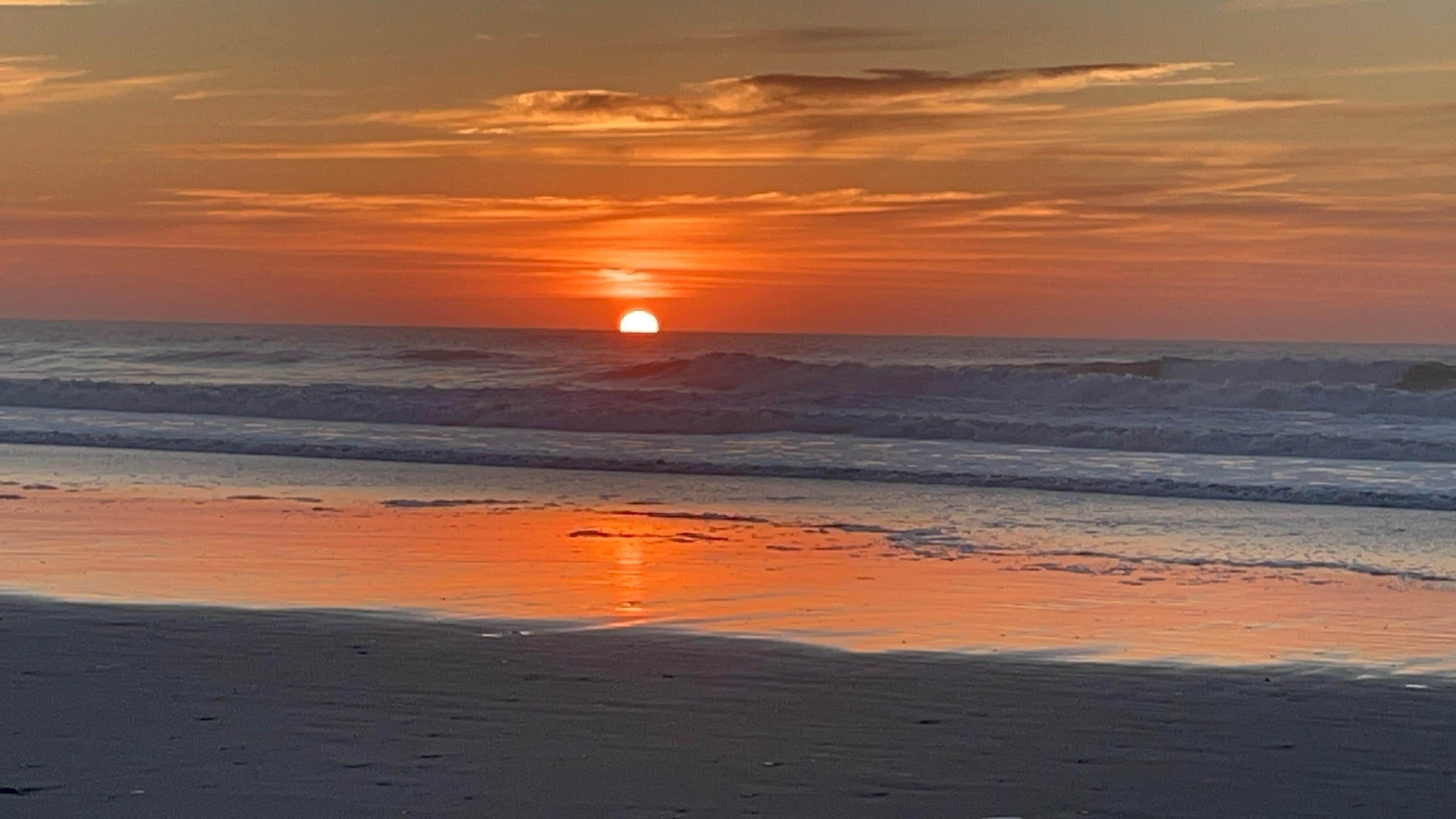A sunset over the ocean with waves approaching the shore.