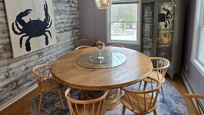 Un comedor con una mesa redonda de cristal, sillas de madera, un muro rústico y un cuadro decorativo con una pintura de cangrejo.