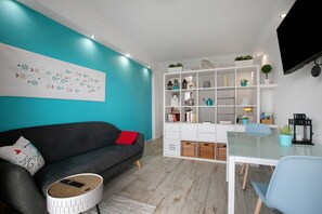 Een moderne woonkamer met een bank, een salontafel, een glazen eettafel en een wit kastenmeubel met decoratieve objecten.