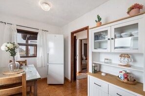 Une cuisine équipée d’un réfrigérateur, d’une table à manger avec des chaises, d’une fenêtre avec des rideaux et d’un buffet contenant de la vaisselle.