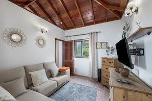 Un salon avec un plafond en bois, un canapé, un téléviseur, un meuble en bois et une fenêtre avec des rideaux.