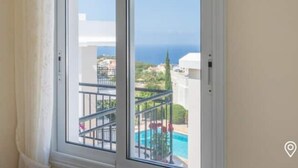 Une fenêtre donnant sur une piscine et un bâtiment à la façade blanche.