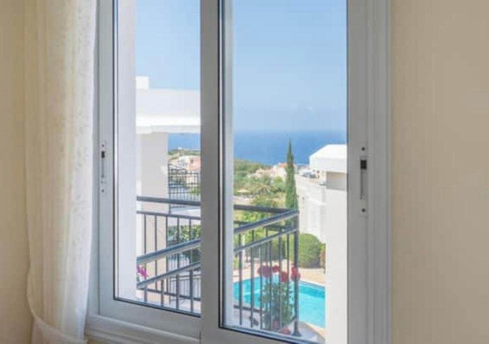 Una ventana con vista a una piscina y un edificio de fachada blanca.