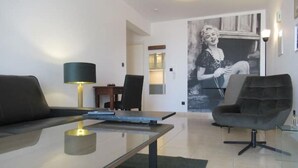 Un salon moderne avec une table basse en verre, un canapé foncé, un fauteuil contemporain et une affiche en noir et blanc accrochée au mur.