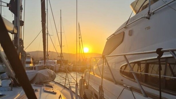 Un port de plaisance où sont amarrés de nombreux yachts, un ciel dégagé et le soleil qui se couche à l’horizon.