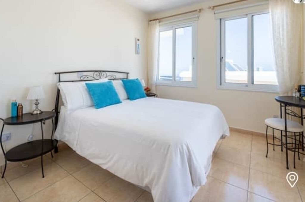 A hotel room with a bed, a small table with a lamp, and a window with curtains.