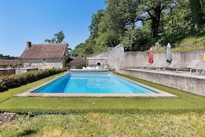 Una piscina rectangular con un muro de piedra y una zona con césped.