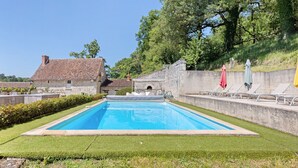 A rectangular swimming pool with a stone wall and a grassy area in front.