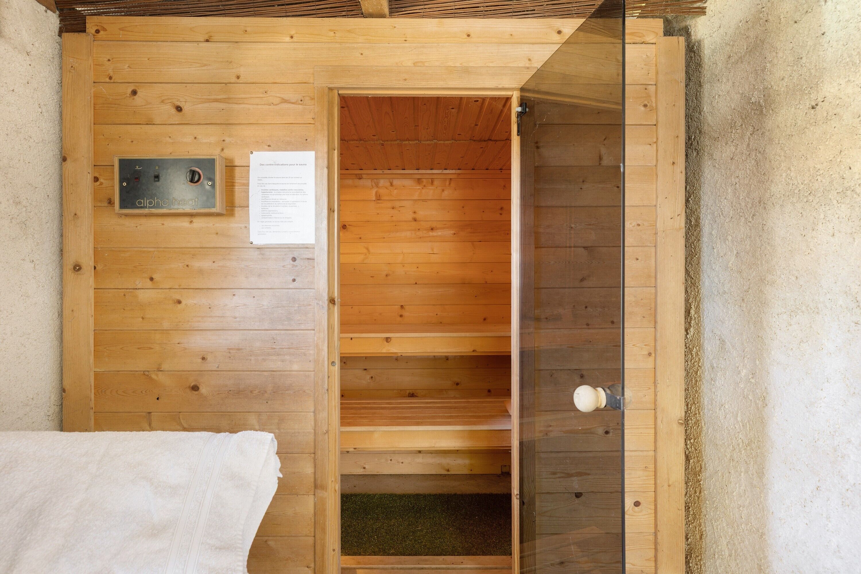 Un sauna de madera con puerta, panel de control y una toalla en el suelo.